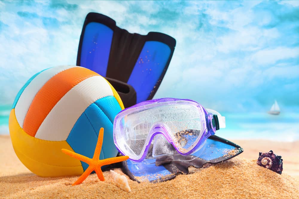 Multioloured plastic beach ball with goggles and flippers lying on the golden sand of a tropical beach on a hot summer day