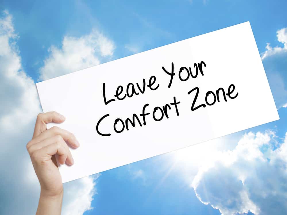 Leave Your Comfort Zone Sign on white paper. Man Hand Holding Paper with text. Isolated on sky background.   Business concept. Stock Photo